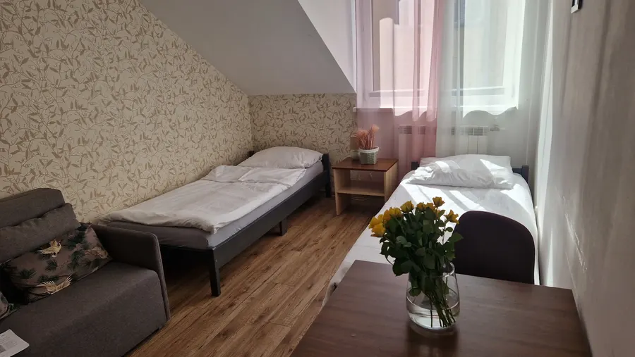 Pokój trzyosobowy z sofą, dwoma łóżkami i stolikiem pod skosem