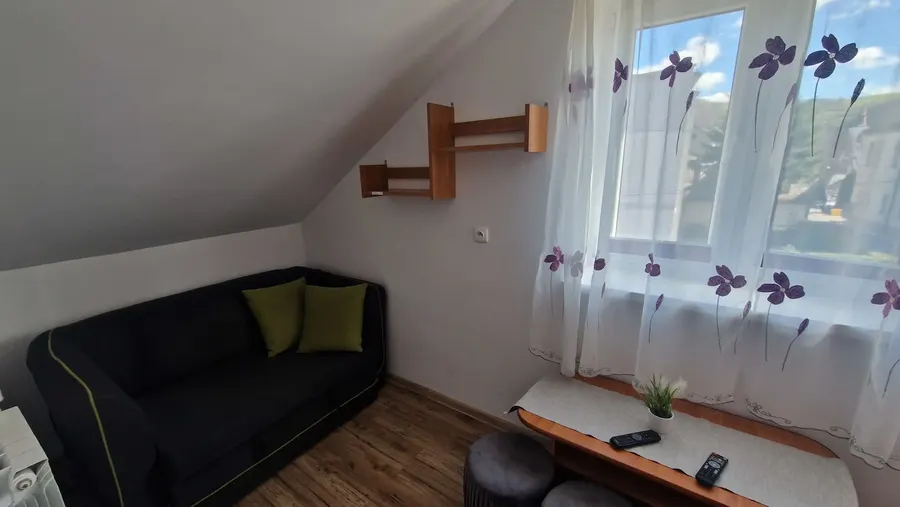 Pokój z sofą pod skosem i widokiem na zielone wzgórza